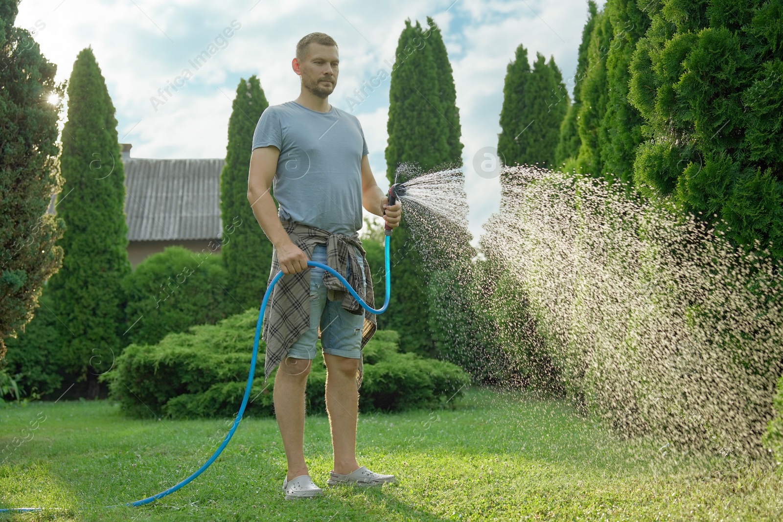 Photo of Man watering lawn with hose in backyard