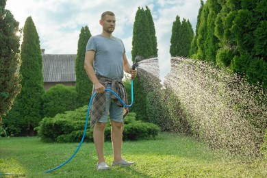 Photo of Man watering lawn with hose in backyard