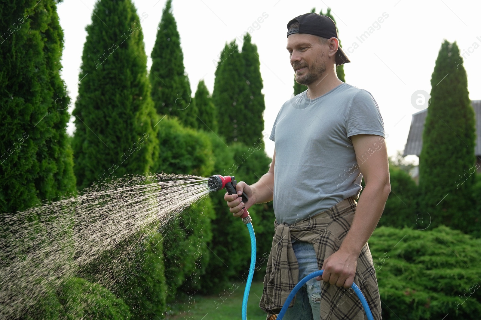 Photo of Man watering lawn with hose in backyard