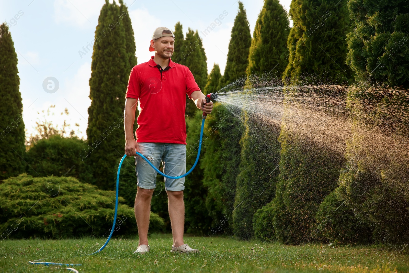 Photo of Man watering lawn with hose in backyard