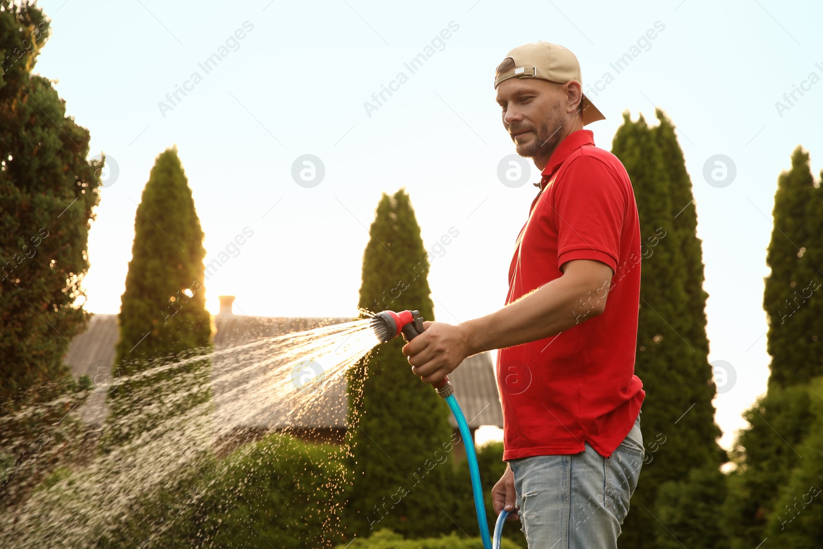 Photo of Man watering lawn with hose in backyard on sunny day