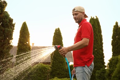 Man watering lawn with hose in backyard on sunny day