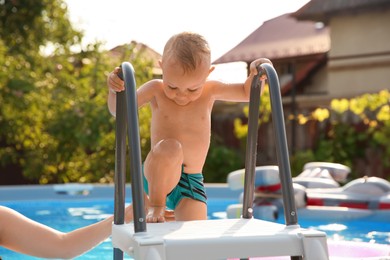 Photo of Little boy getting out of swimming pool by ladder outdoors