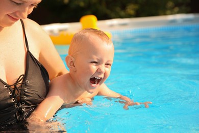 Photo of Mother and her son having fun in swimming pool outdoors, space for text