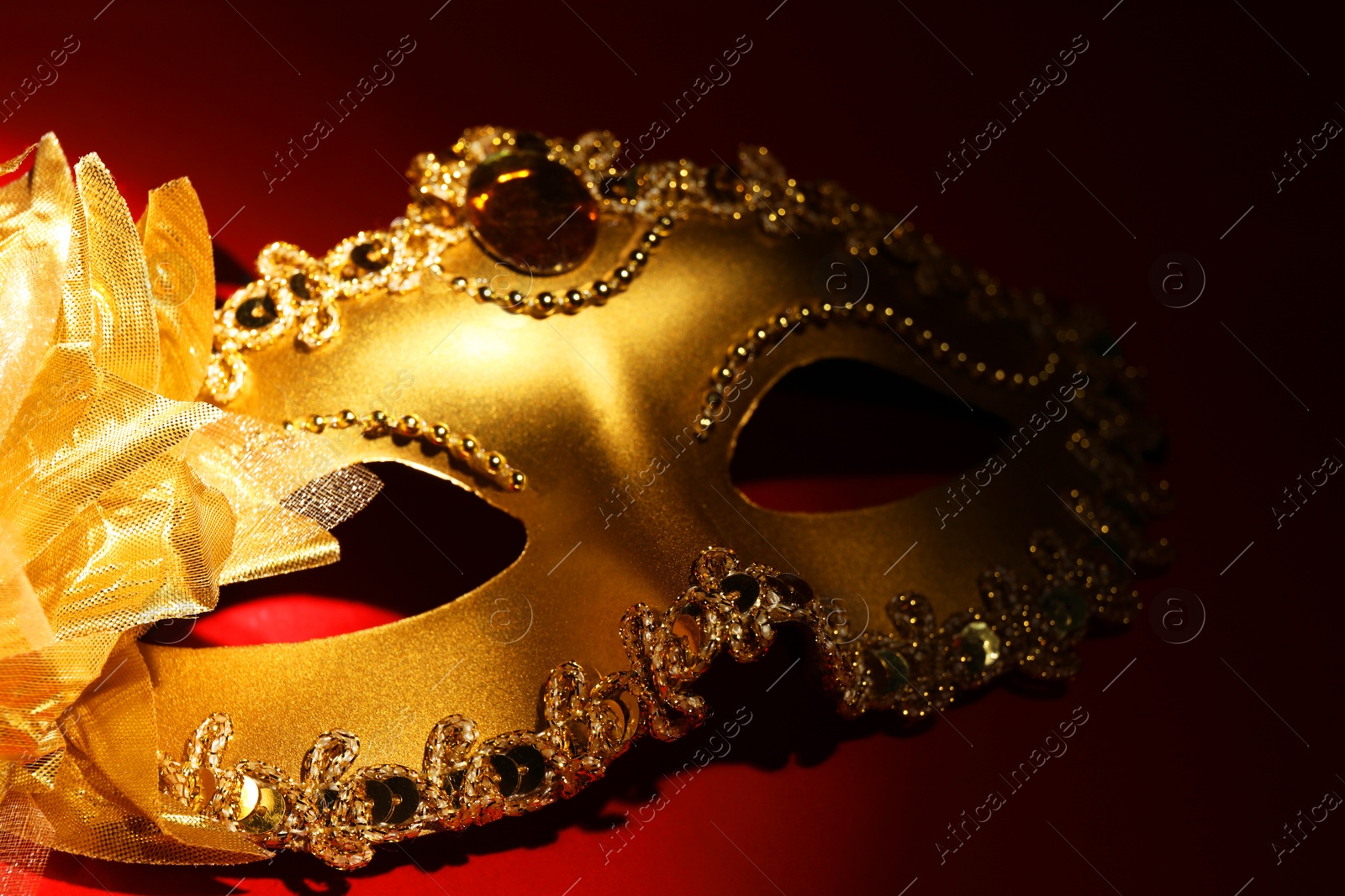 Photo of Beautiful golden carnival mask on red background, closeup