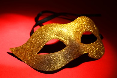 Photo of Beautiful golden carnival mask on red background, closeup