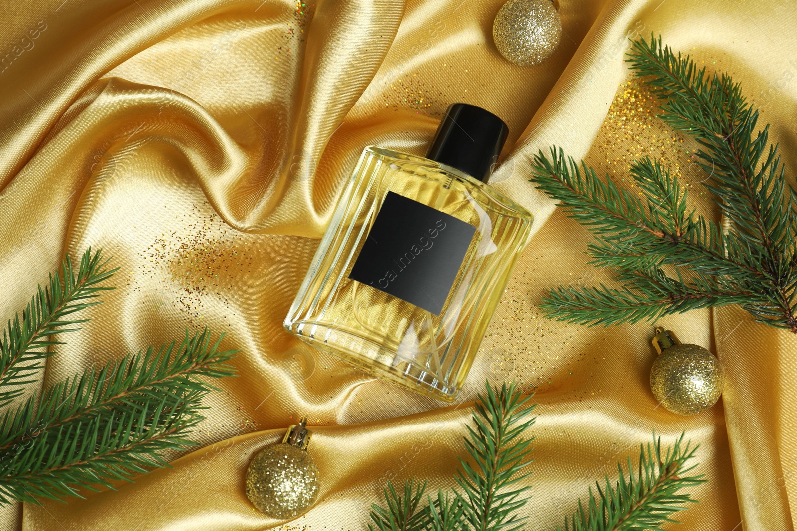 Photo of Christmas composition with perfume bottle on golden fabric, flat lay