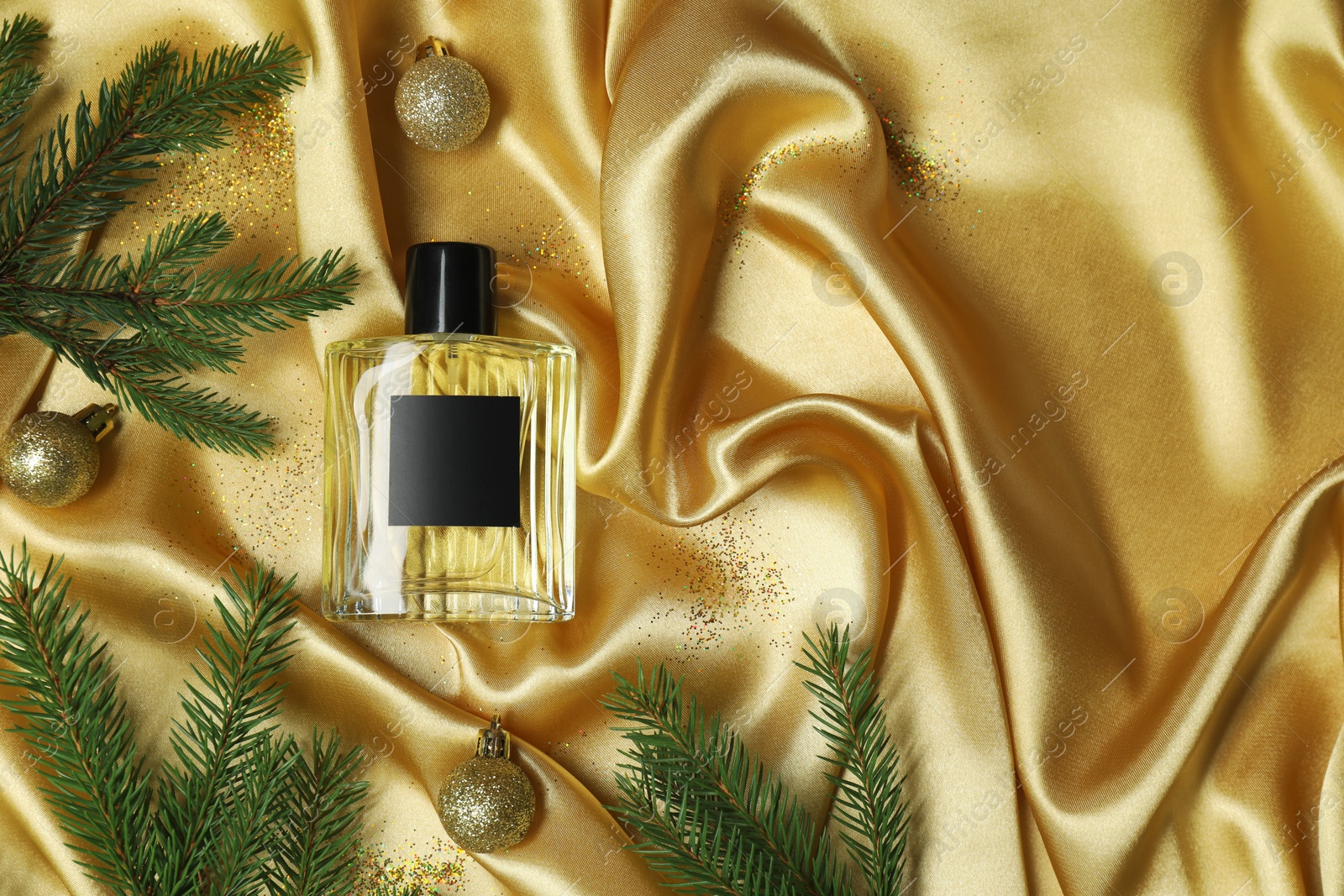 Photo of Christmas composition with perfume bottle on golden fabric, flat lay. Space for text