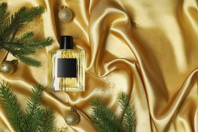 Christmas composition with perfume bottle on golden fabric, flat lay. Space for text