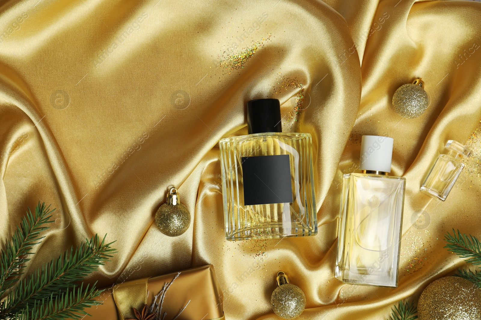 Photo of Christmas composition with perfume bottles on golden fabric, flat lay. Space for text