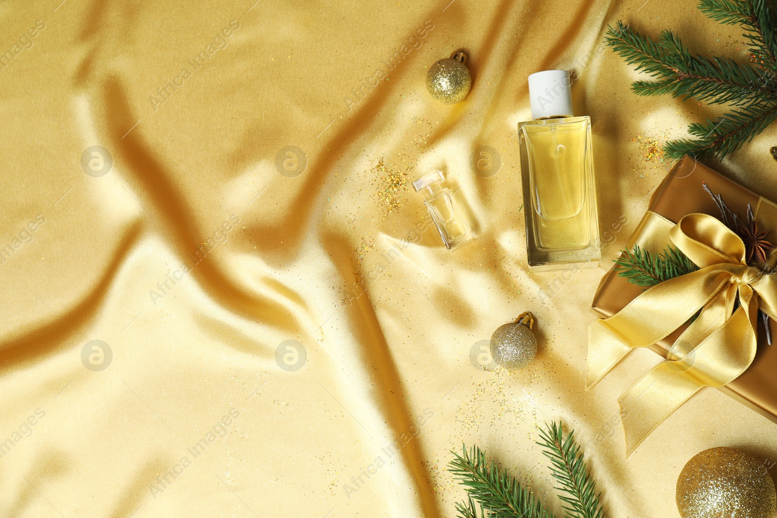 Photo of Christmas composition with perfume bottle on golden fabric, flat lay. Space for text