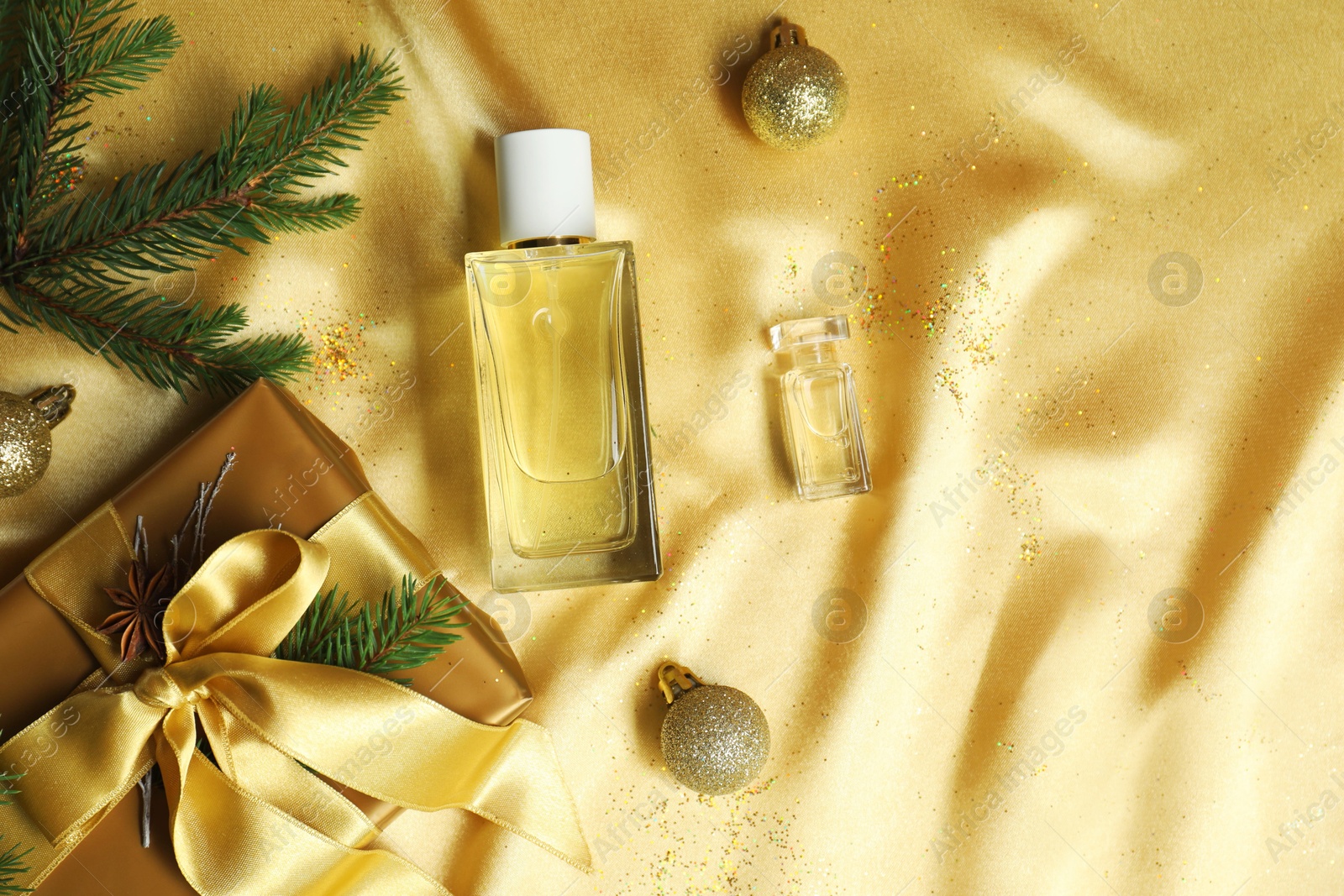 Photo of Christmas composition with perfume bottles on golden fabric, flat lay