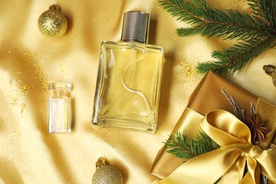 Photo of Christmas composition with perfume bottles on golden fabric, flat lay