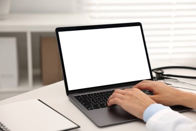 Photo of Doctor using laptop at white table in hospital, closeup