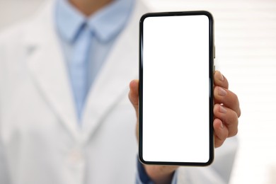 Photo of Doctor showing smartphone with blank screen in hospital, selective focus