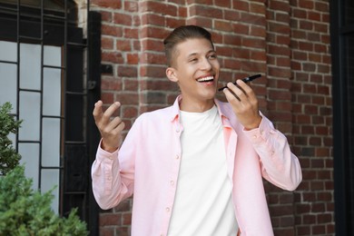 Young man recording voice message via smartphone outdoors