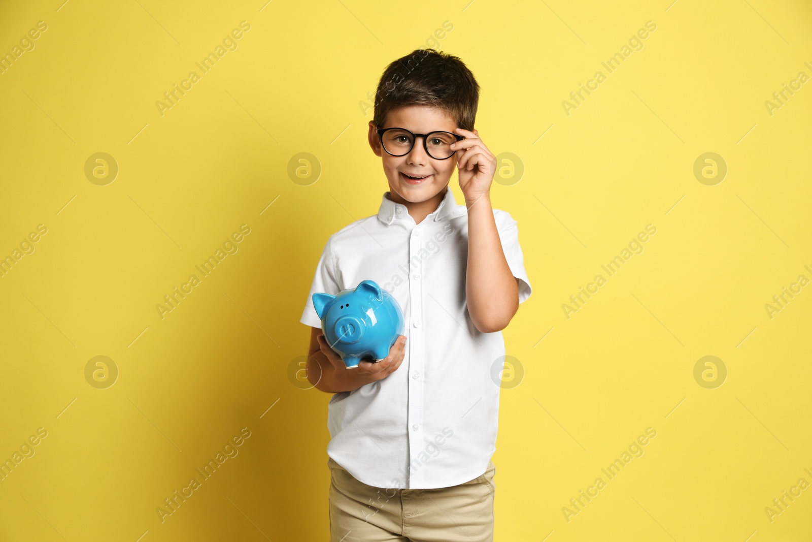 Photo of Pocket money. Cute boy with piggy bank on yellow background