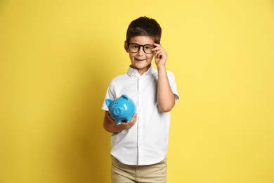 Photo of Pocket money. Cute boy with piggy bank on yellow background