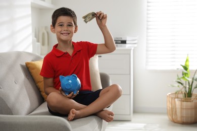 Cute boy with piggy bank and pocket money on sofa at home, space for text