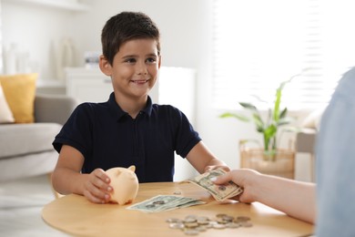 Photo of Mother giving pocket money to her son at table indoors