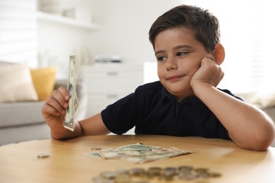 Cute boy with pocket money at wooden table indoors