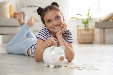 Photo of Pocket money. Cute girl putting coin into piggy bank at home, space for text