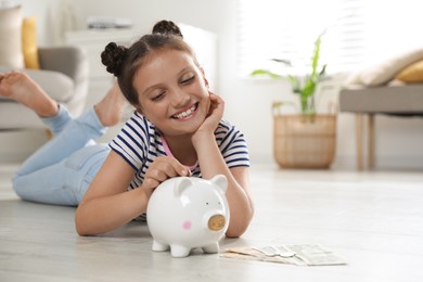 Pocket money. Cute girl putting coin into piggy bank at home, space for text