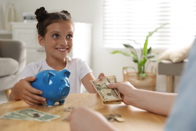 Mother giving pocket money to her daughter at table indoors