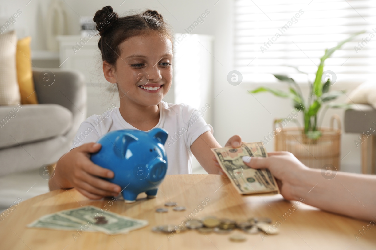 Photo of Mother giving pocket money to her daughter at table indoors