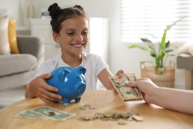 Mother giving pocket money to her daughter at table indoors