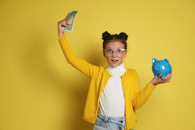 Photo of Pocket money. Cute girl with piggy bank and dollar banknotes on yellow background