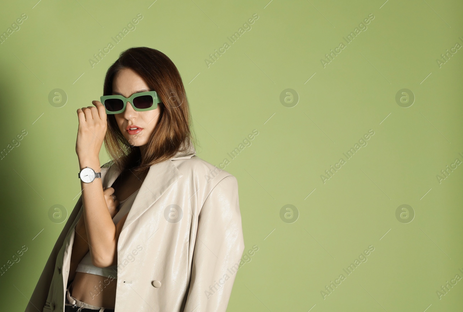 Photo of Beautiful woman in stylish beige suit and sunglasses on olive background, space for text