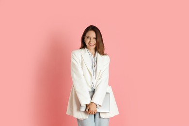 Beautiful woman in stylish white jacket with laptop on pink background