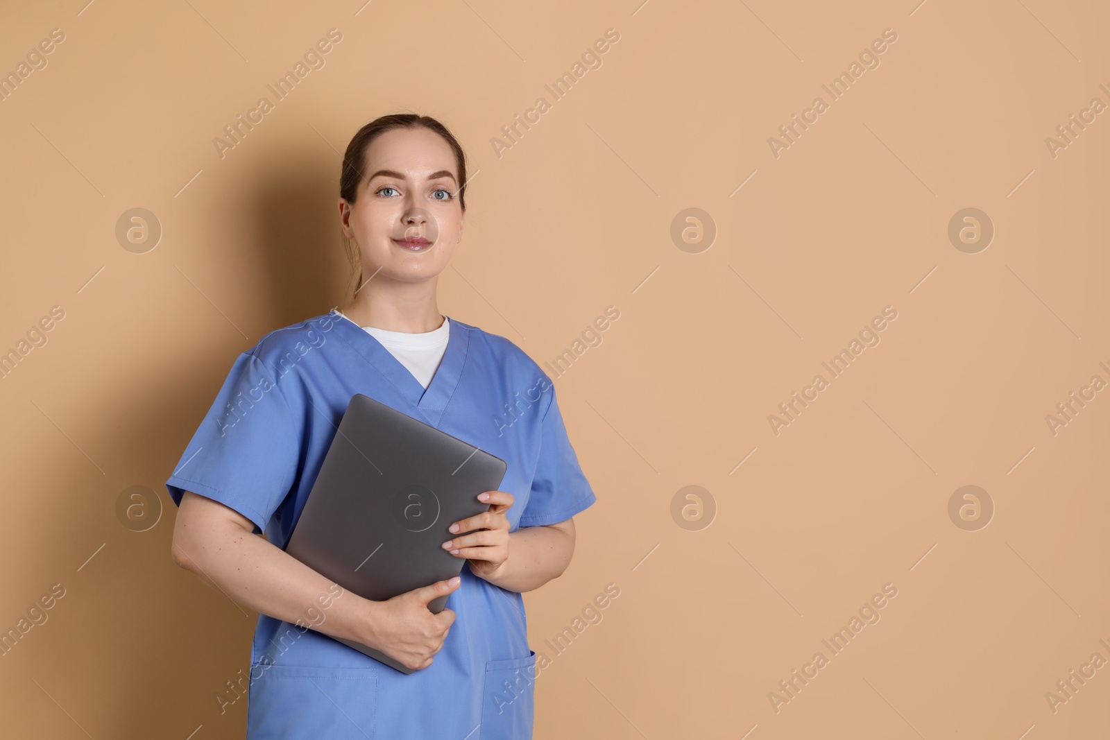 Photo of Portrait of nurse with laptop on dark beige background. Space for text