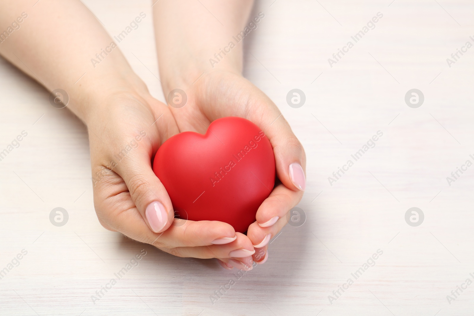 Photo of Woman with red decorative heart at white wooden table, closeup