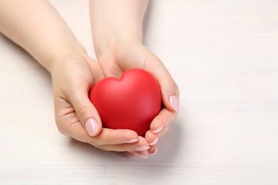 Photo of Woman with red decorative heart at white wooden table, closeup