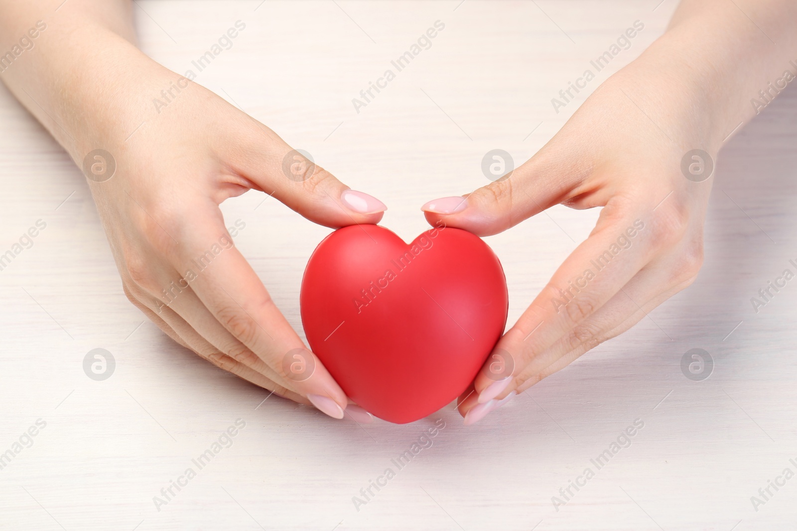 Photo of Woman with red decorative heart at white wooden table, closeup