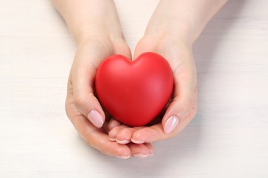 Photo of Woman with red decorative heart at white wooden table, closeup