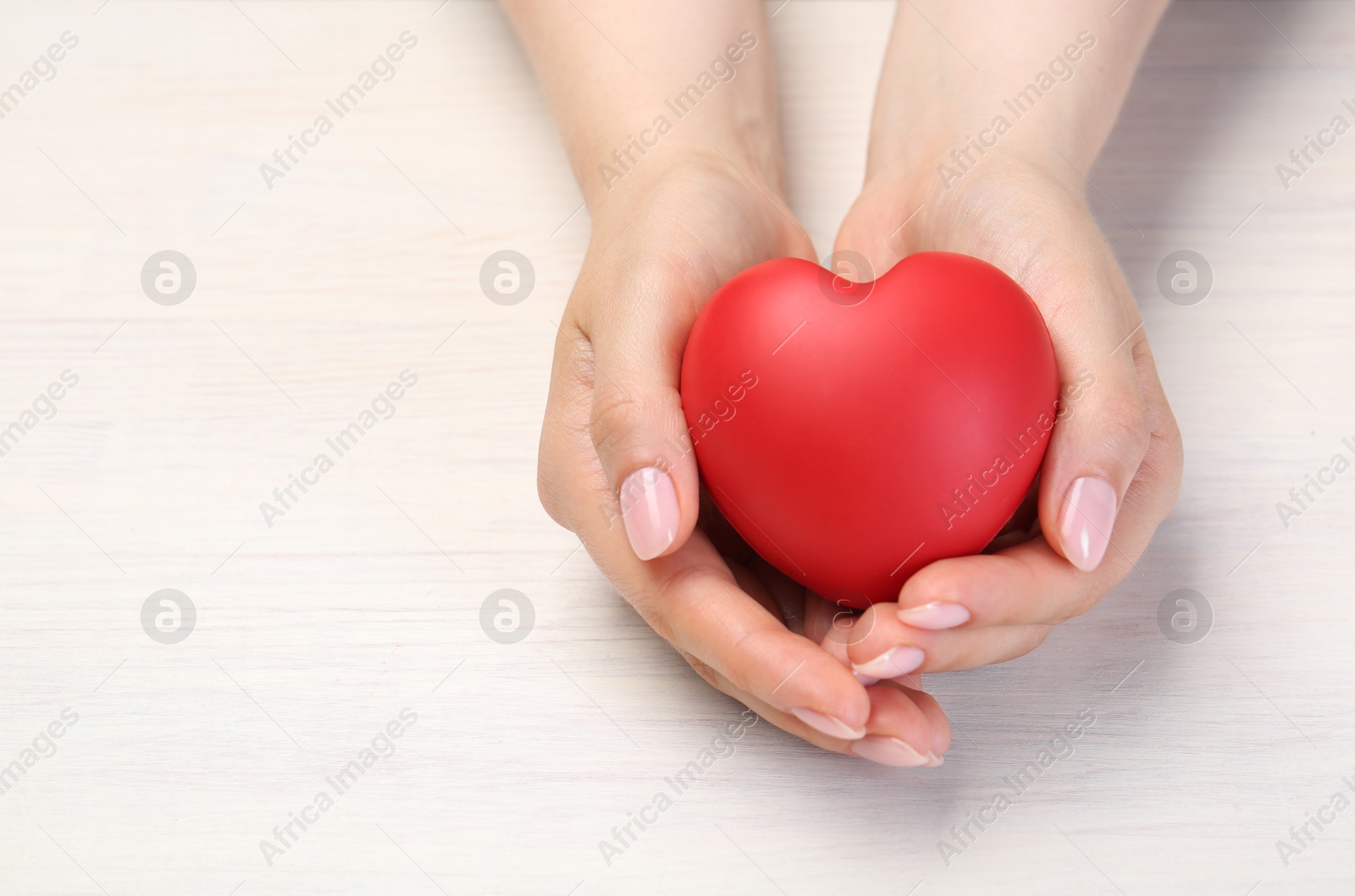 Photo of Woman with red decorative heart at white wooden table, closeup. Space for text