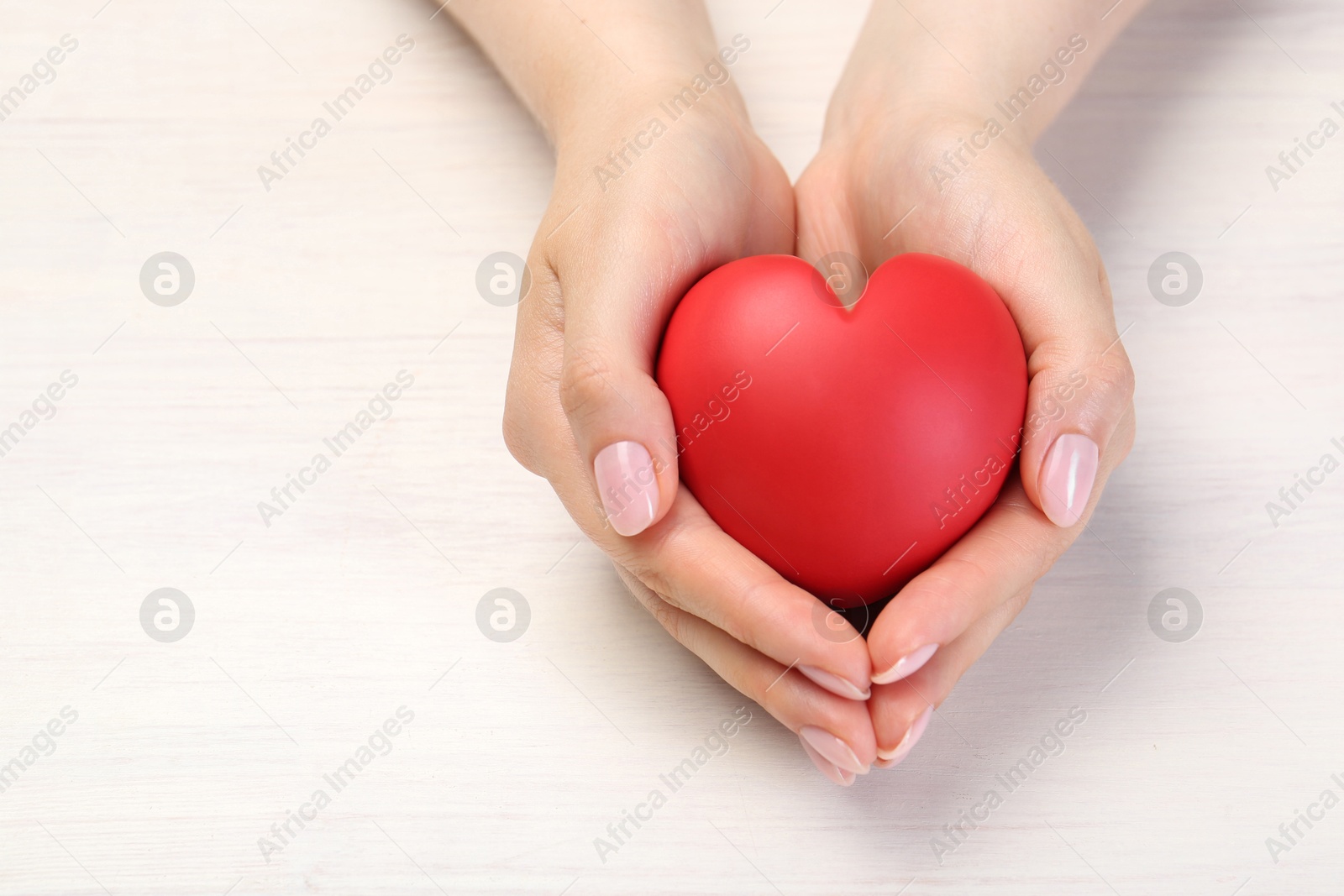 Photo of Woman with red decorative heart at white wooden table, closeup. Space for text