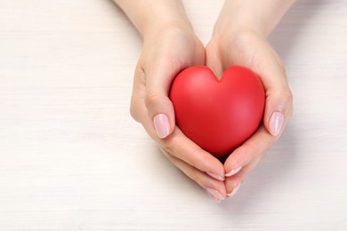 Woman with red decorative heart at white wooden table, closeup. Space for text