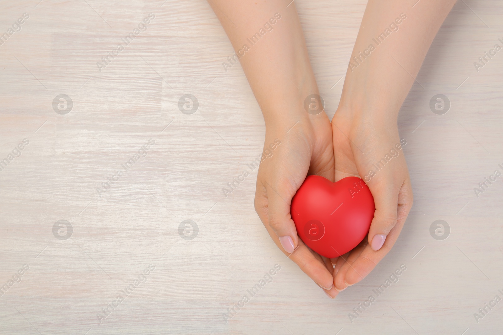 Photo of Woman with red decorative heart at white wooden table, top view. Space for text