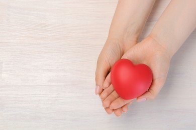 Photo of Woman with red decorative heart at white wooden table, top view. Space for text