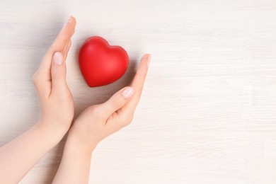 Photo of Woman with red decorative heart at white wooden table, top view. Space for text