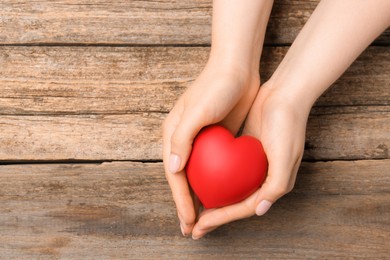 Photo of Woman with red decorative heart at wooden table, top view. Space for text