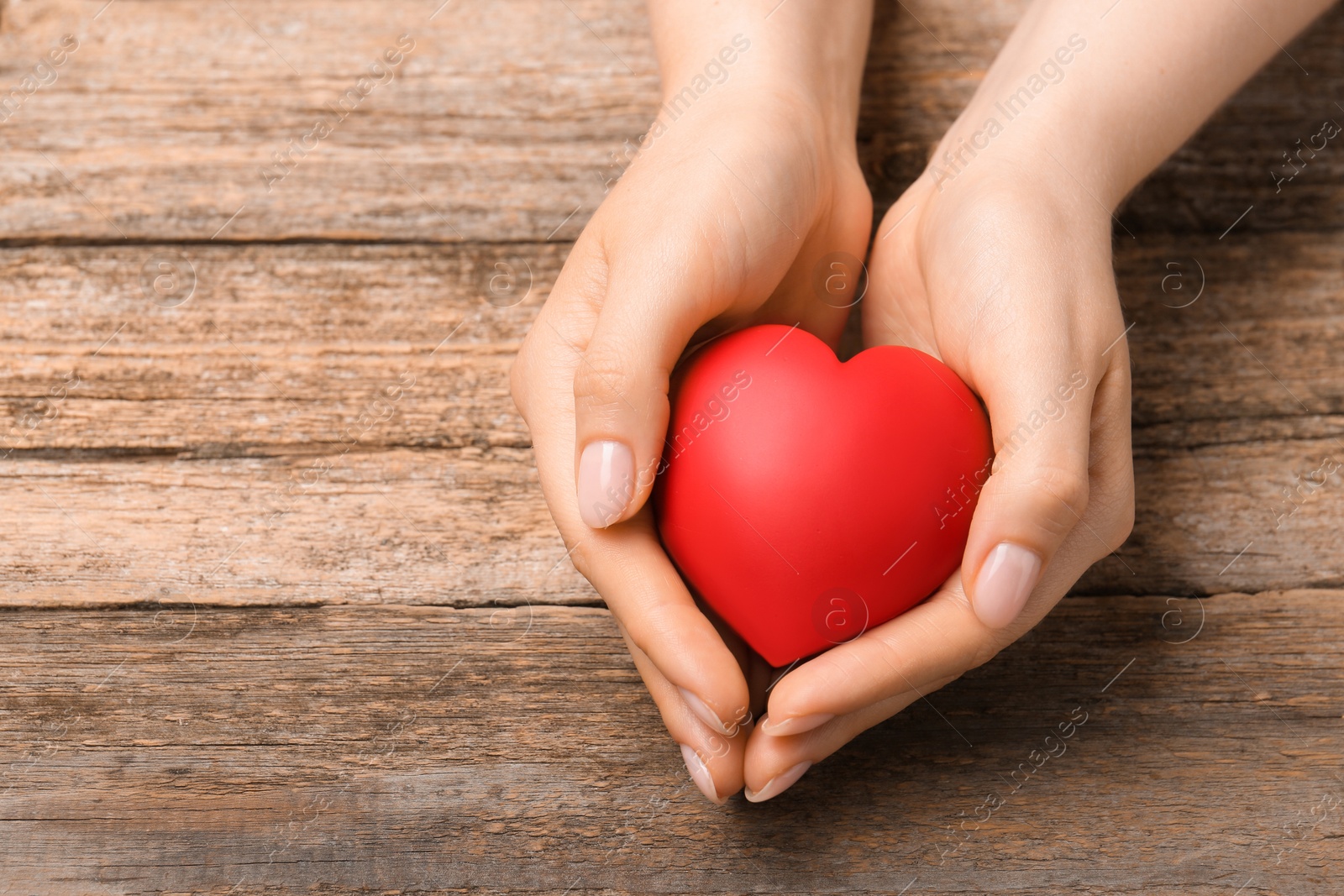 Photo of Woman with red decorative heart at wooden table, closeup. Space for text