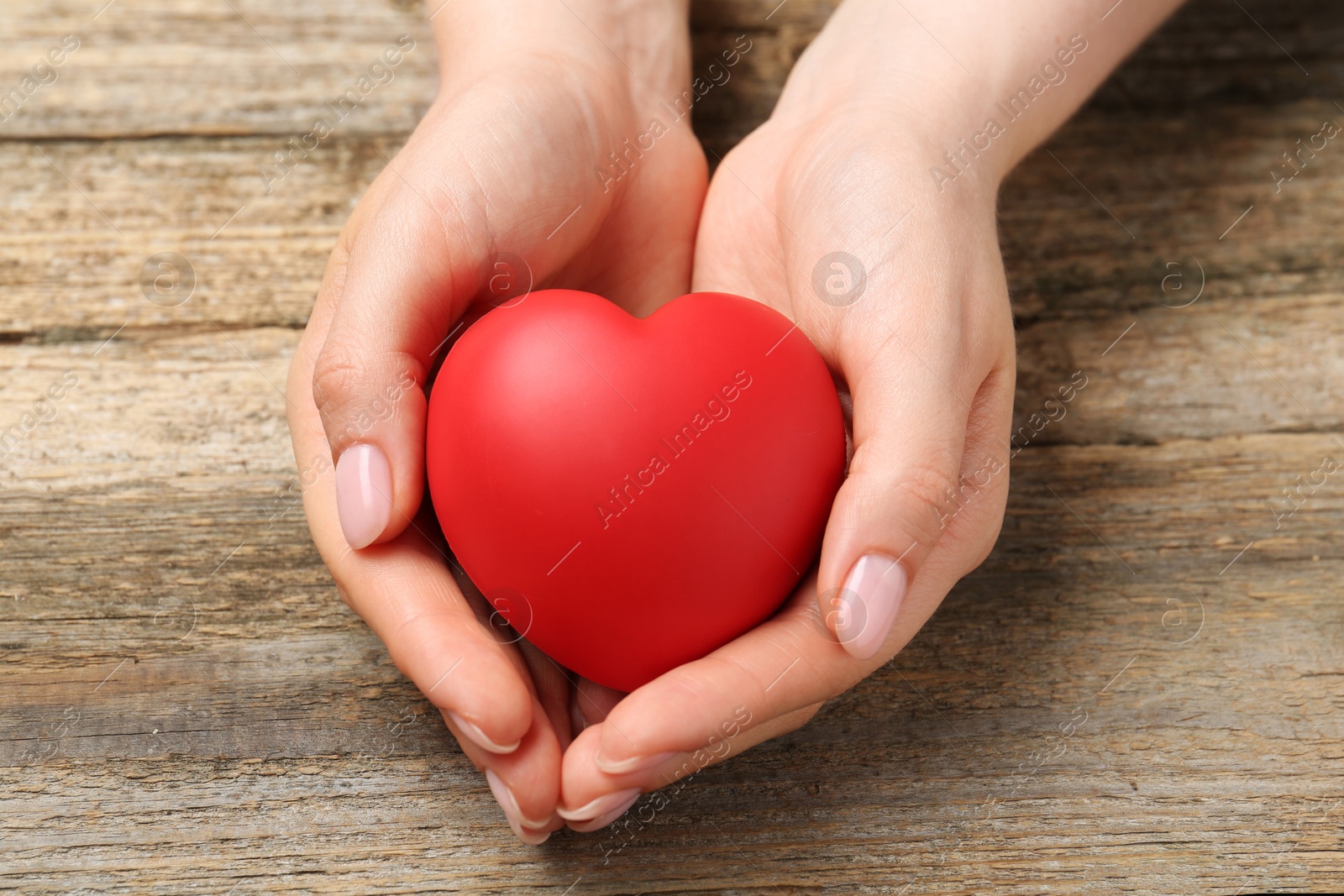 Photo of Woman with red decorative heart at wooden table, closeup