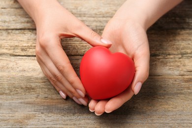 Photo of Woman with red decorative heart at wooden table, closeup