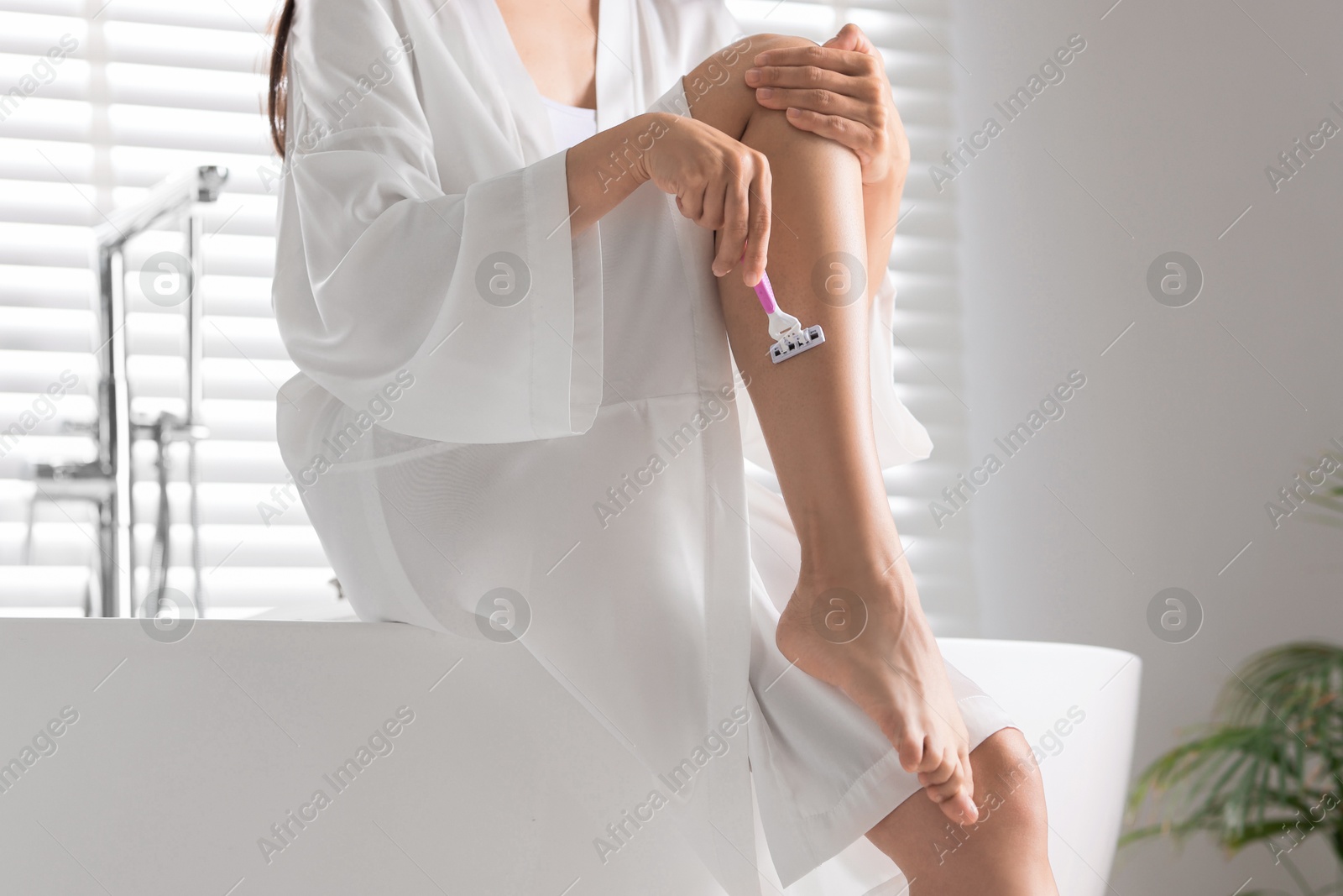 Photo of Woman shaving leg on bathtub in bathroom, closeup