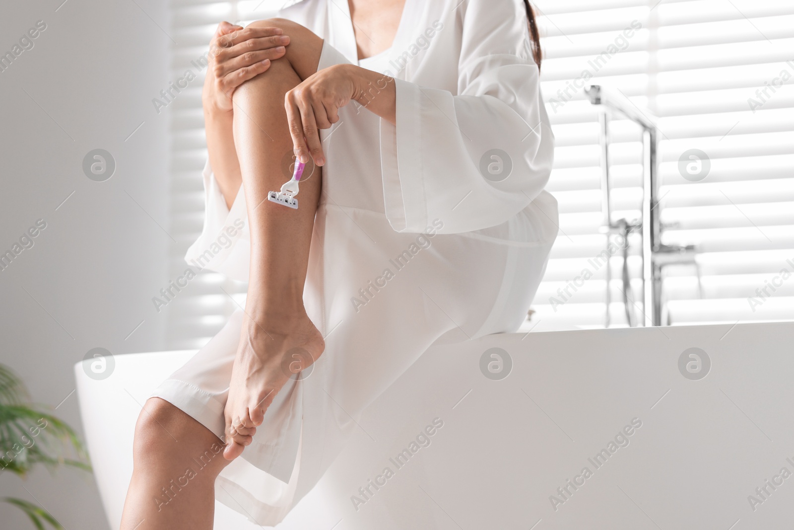 Photo of Woman shaving leg on bathtub in bathroom, closeup